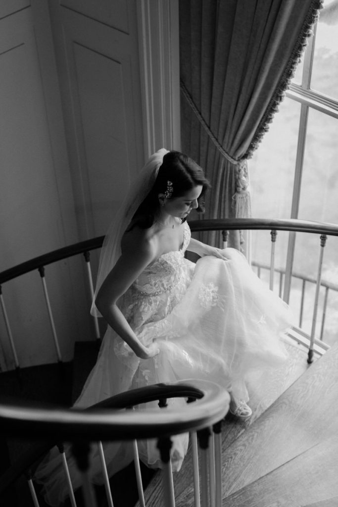 bride holding up the front of her dress while she walks up a spiral staircase