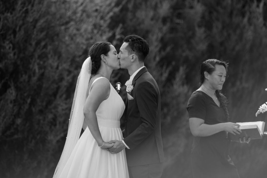 bride and groom during their first kiss with the officiant in the backgorund