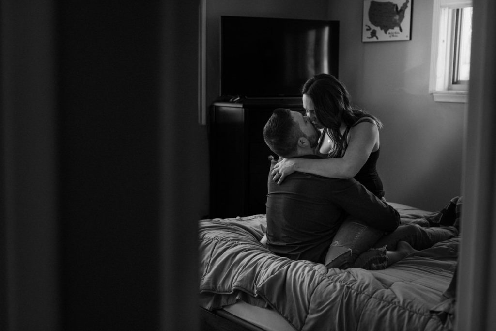 woman sitting on mans lap kissing him on a bed