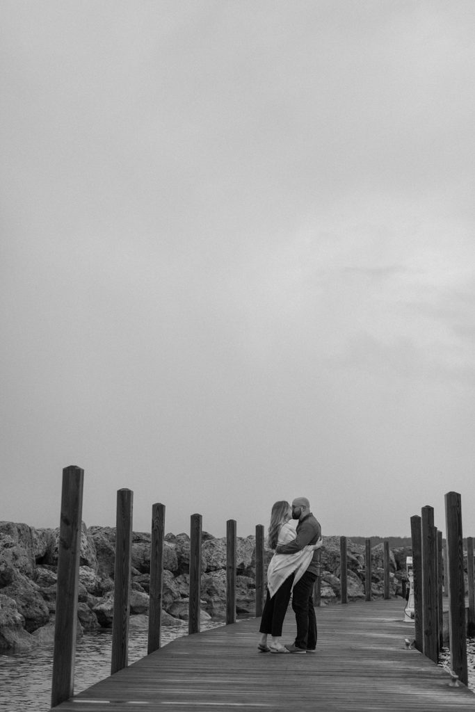 black and white photo of a couple kissing on a pier