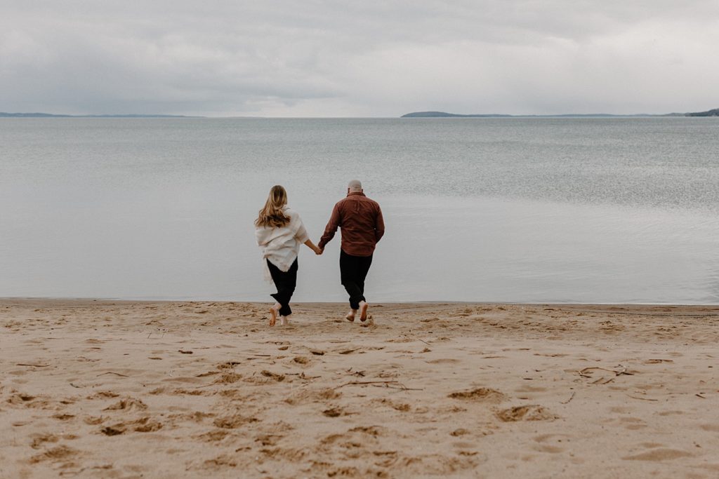couple holding hands and walking towards the water on a beach