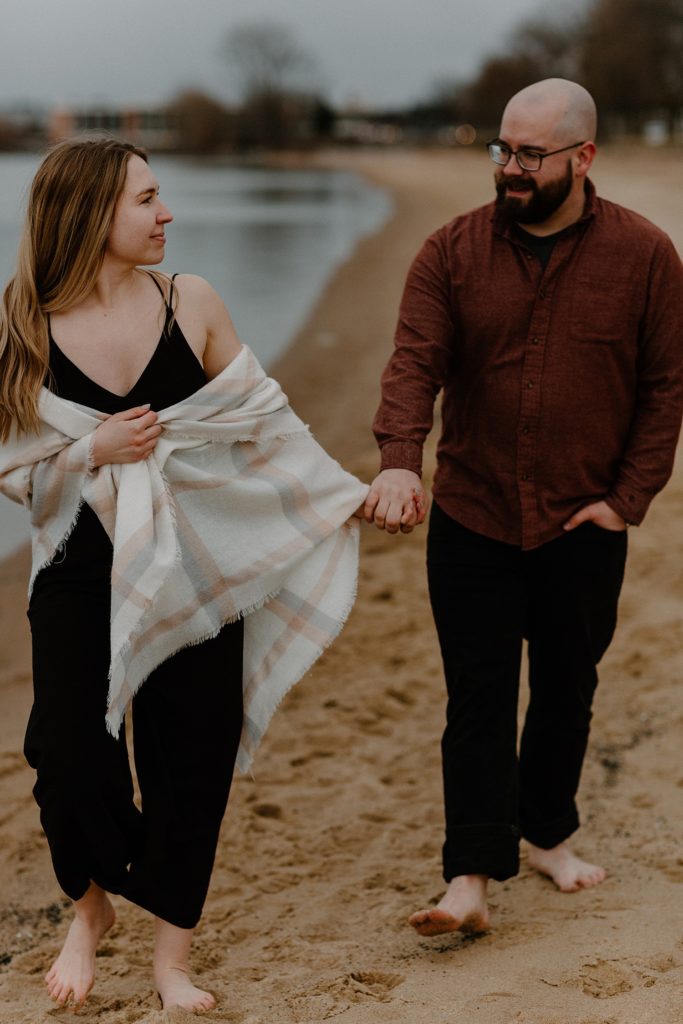 couple holding hands and walking along water line