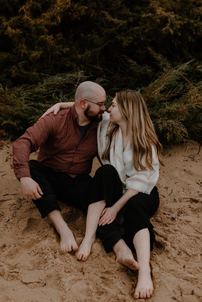 couple sitting next to each other on a beach about to kiss