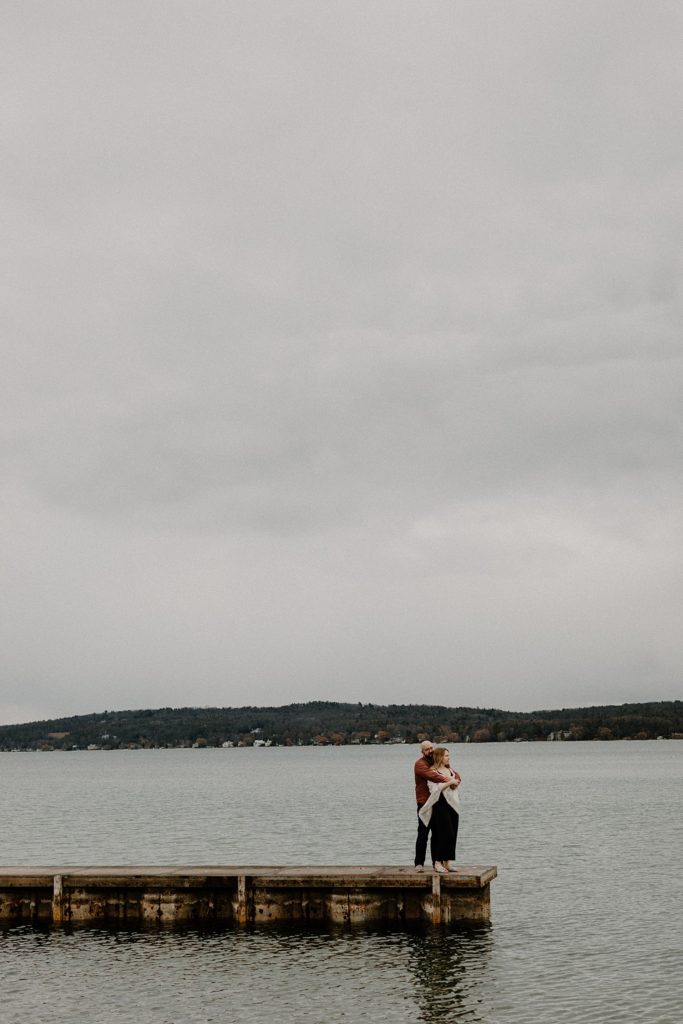 man with his arms around a woman as they stand on the edge of a pier