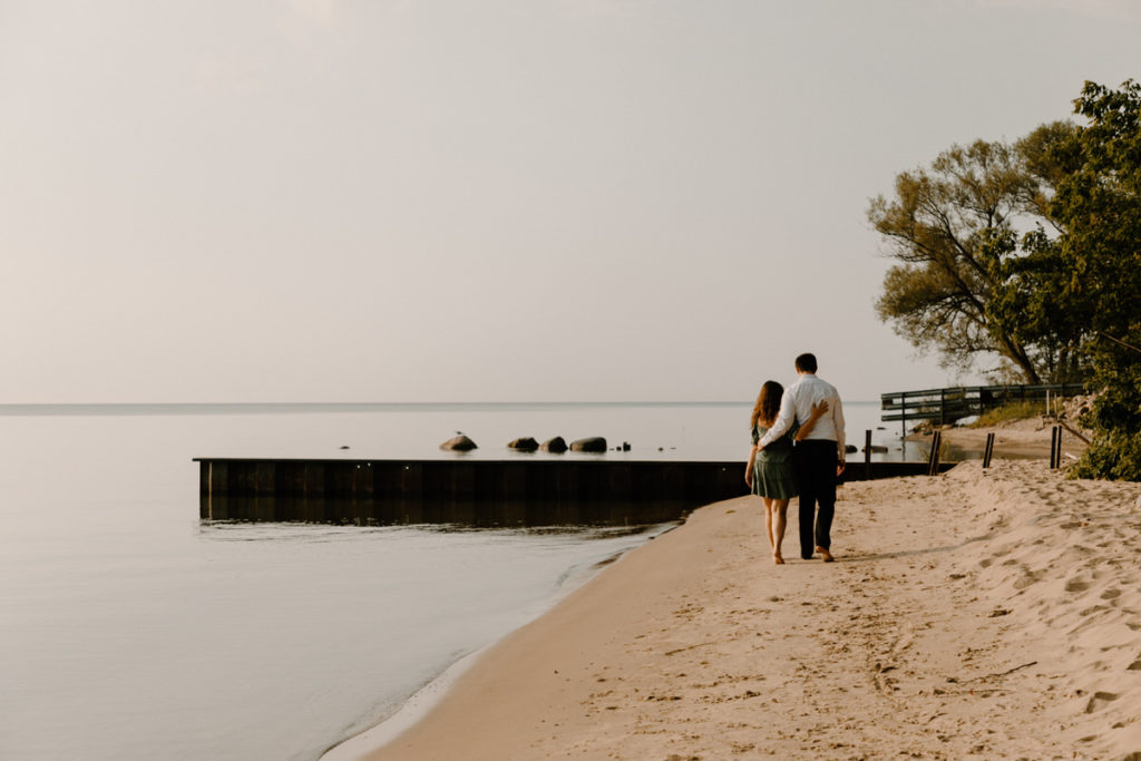 man and woman walking along a sandy beach with their arms around each other