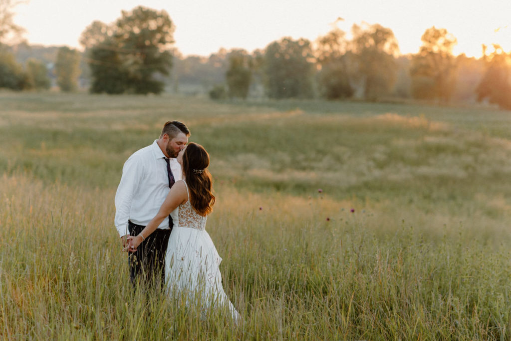 man and women kissing and holding hands in a large field on their wedding day