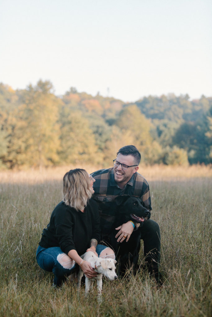 man and woman sitting with their dogs in a field smiling at each other