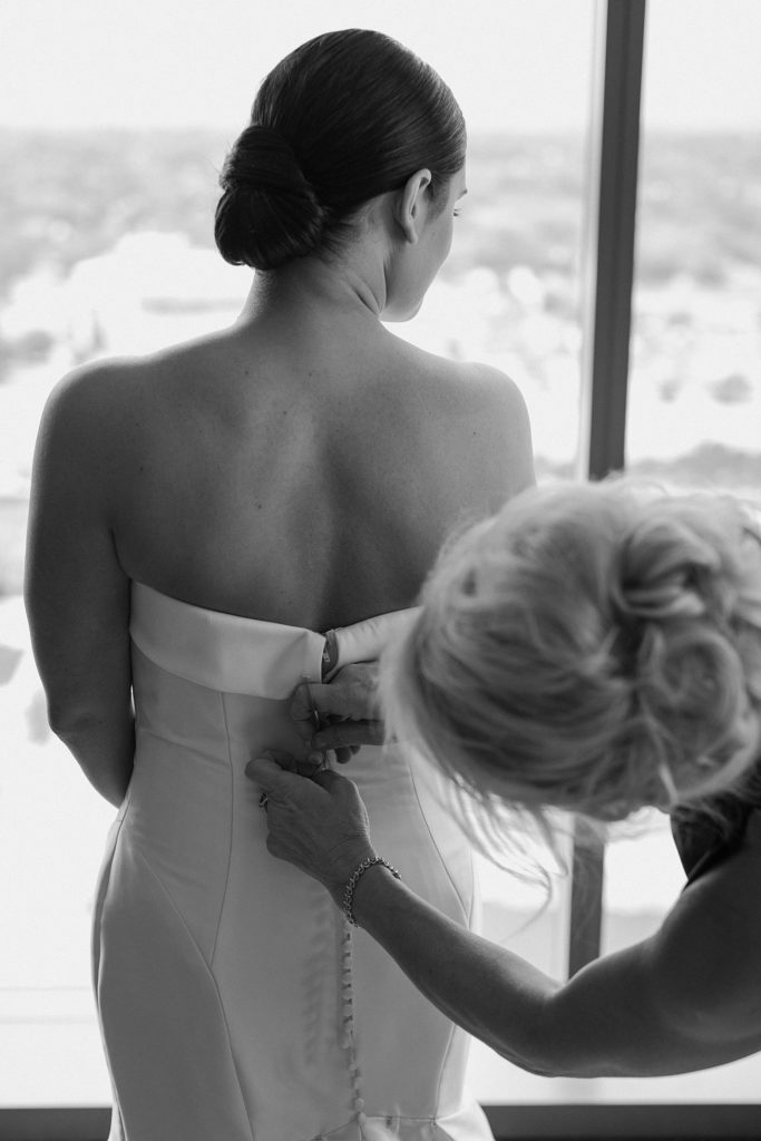 black and white photo of woman zipping up wedding dress 