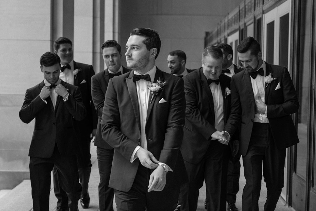 groom adjusting sleeve and looking off with wedding party behind him 