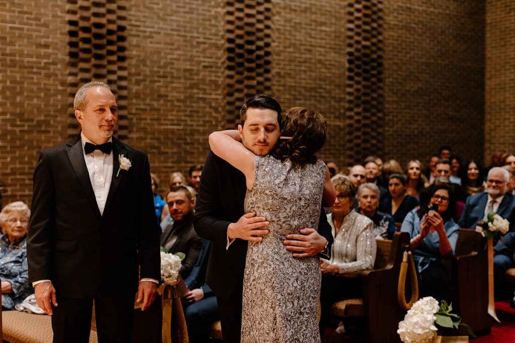 groom hugging mom with guests behind him 