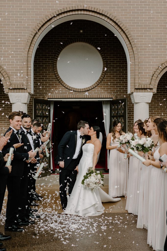 couple kissing with wedding party standing on either side of them 