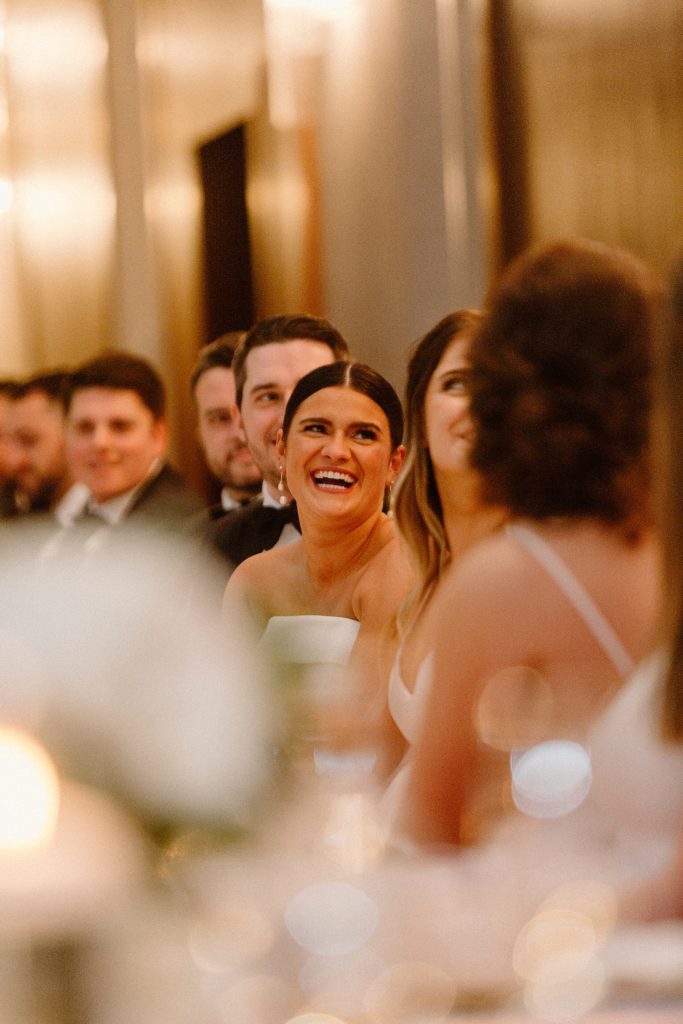 bride smiling while sitting with wedding party 