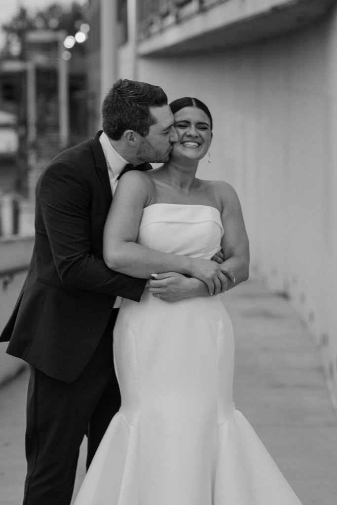 groom kissing bride on the cheek while hugging her from behind 