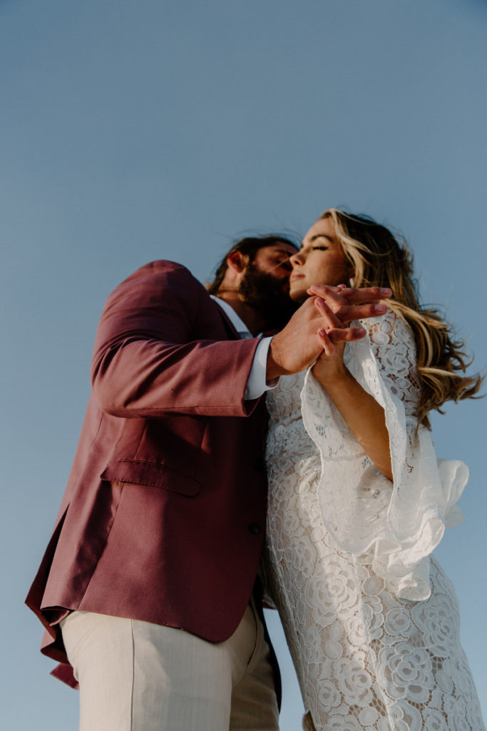 bride and groom holding hands while he kisses her cheek