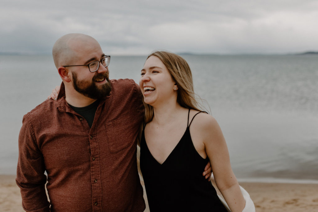 couple standing side by side with their arms around each other at the beach