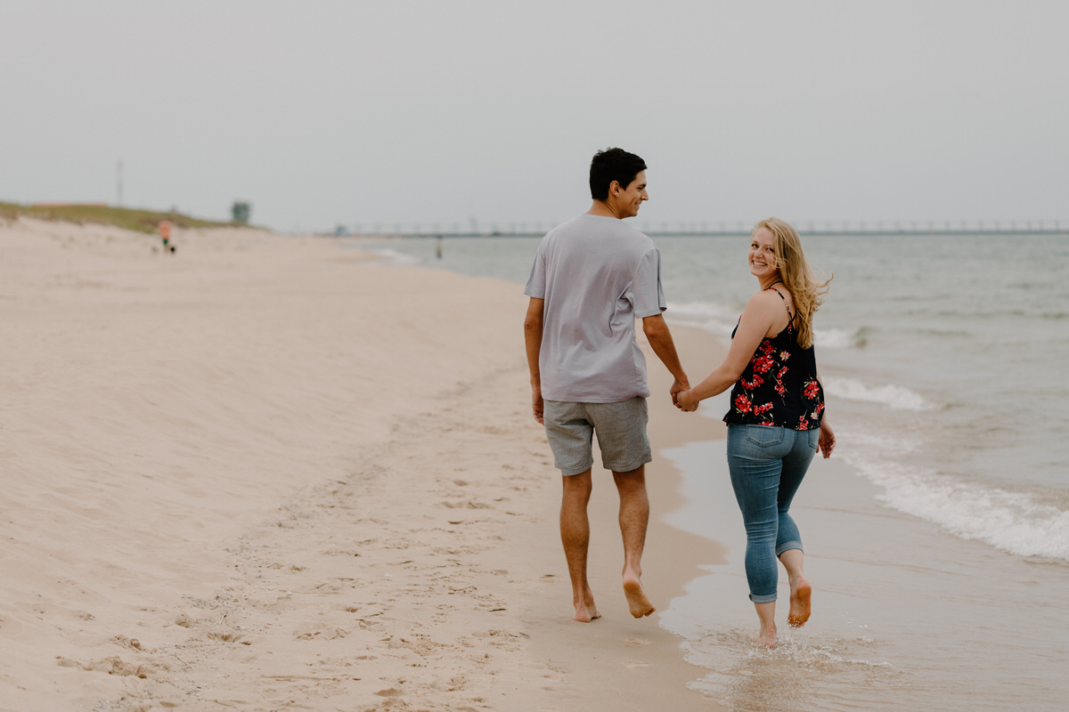 couple walking on water's edge at the beach as the woman looks over her shoulder