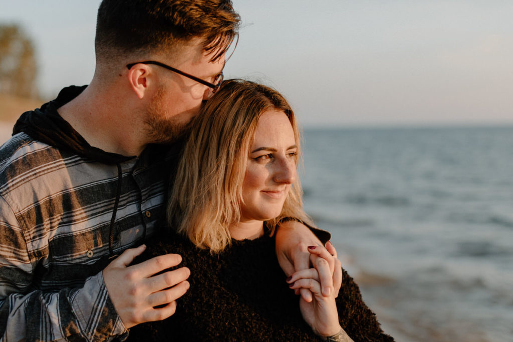 man with his arms around a woman kissing her head on the beach
