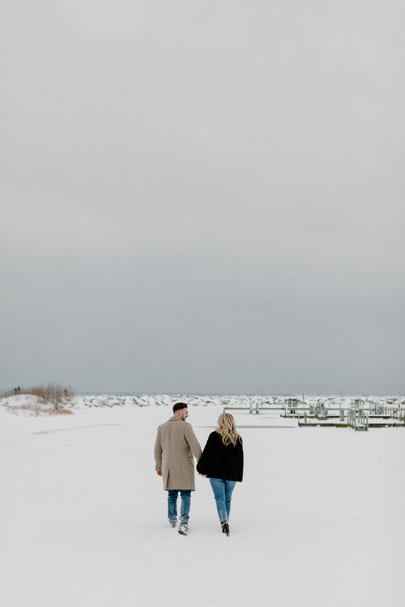 couple holding hands walking along snow covered beach