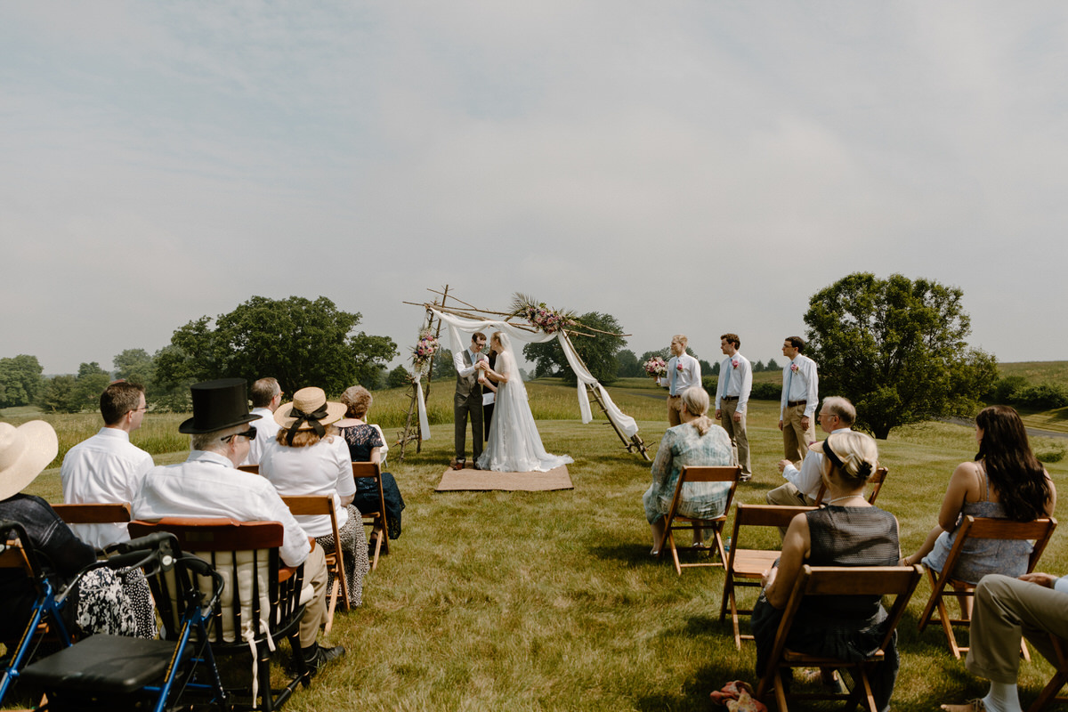 couple under small arch at wedding with a few guests watching