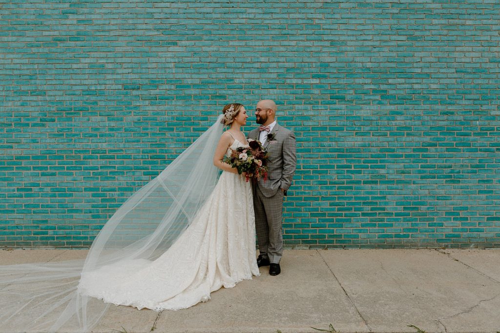 bride and groom standing against a teal brick wall