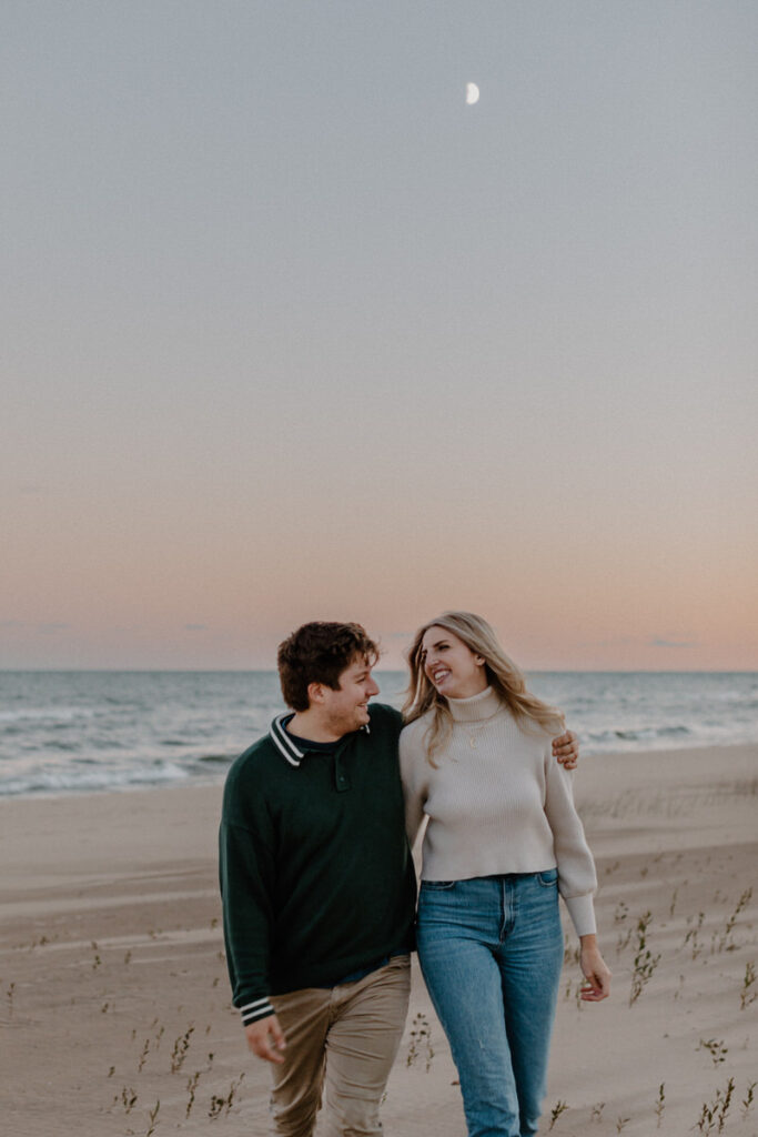 couple with their arms around each other walking along the beach at sunset