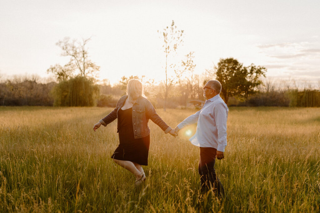 couple in a field at sunset holding hands as one of them skips