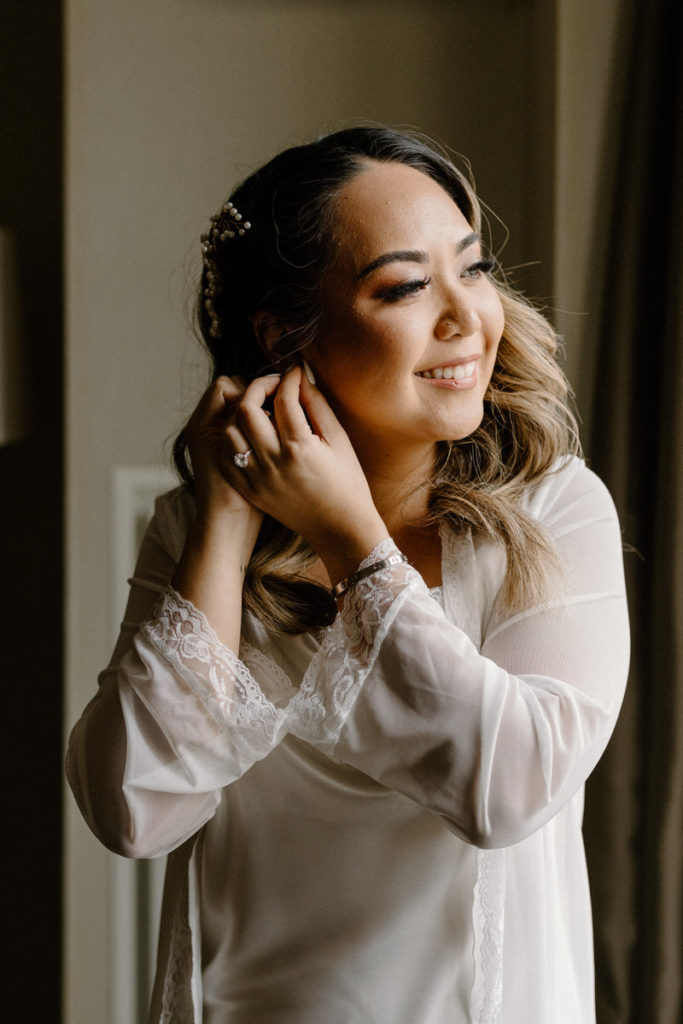 bride smiling and looking off to the side as she puts in an earring