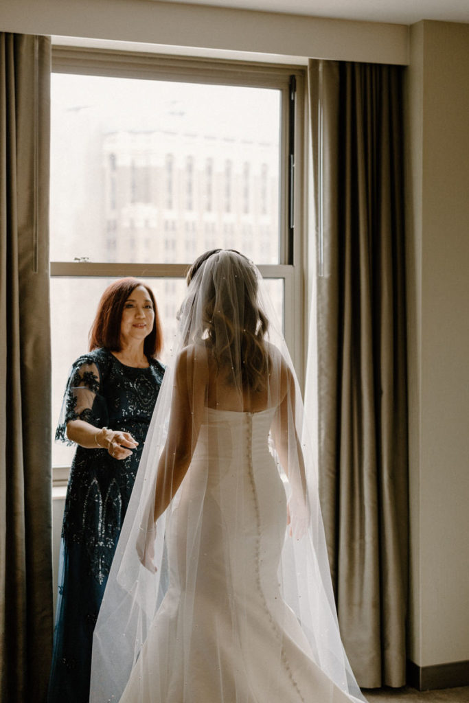 a mother standing in front of her daughter in a wedding dress smiling