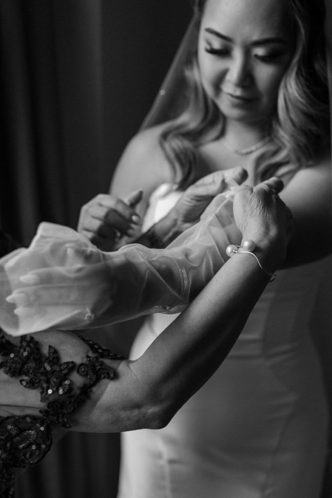 black and white photo of a woman helping a bride put on a long, see through glove