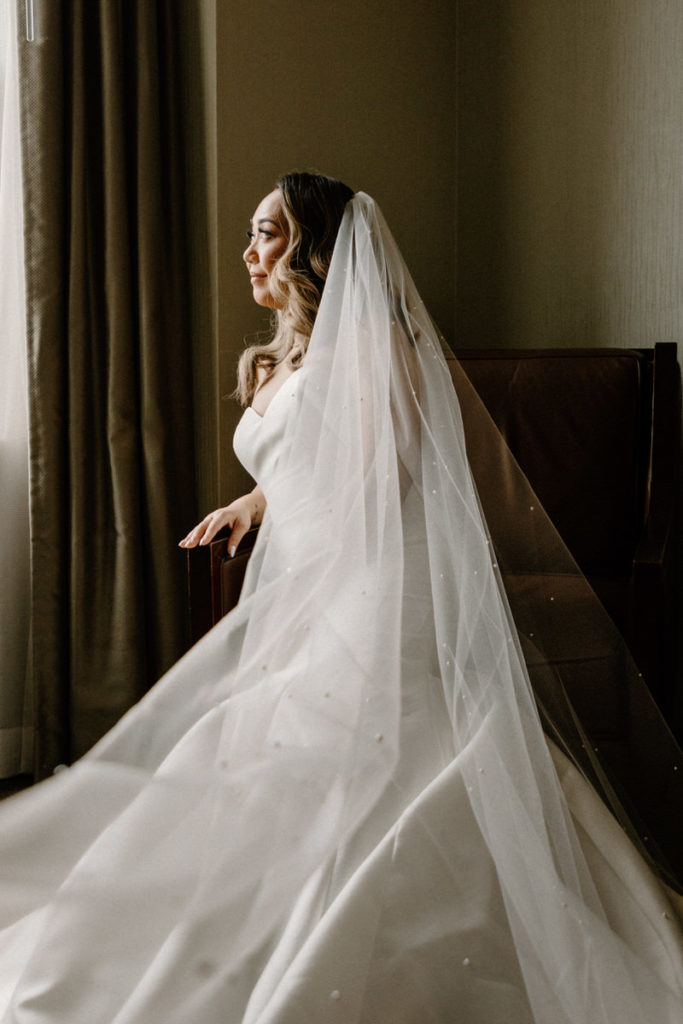 getting ready wedding photo of a bride in her wedding dress looking out a window