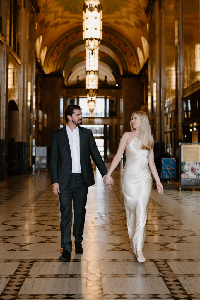 couple in cocktail attire holding hands and walking in an art deco building