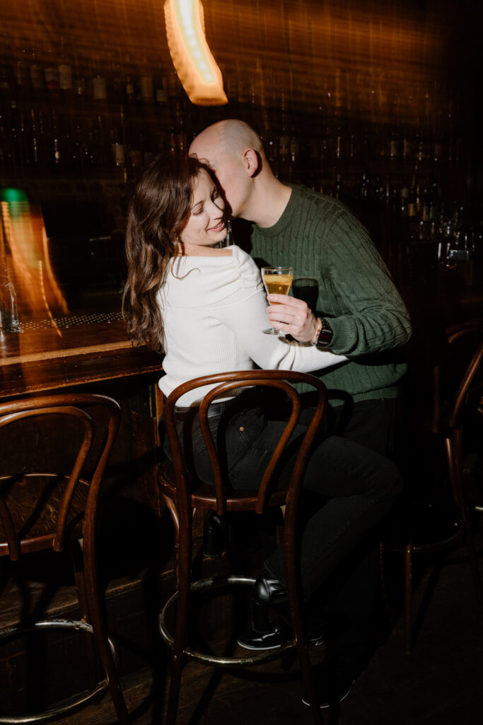 couple embracing while holding cocktails and sitting at a bar